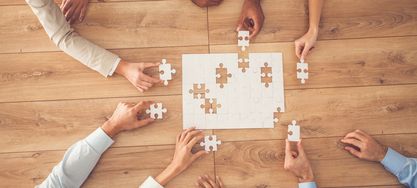 Geschäftsleute sitzen am Schreibtisch, setzen Puzzleteile zusammen, finden eine Lösung, hohe Winkelansicht.