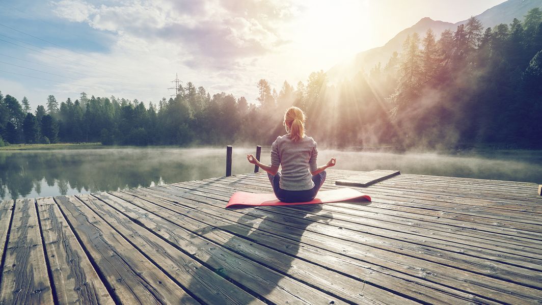 Eine Frau macht Yoga auf einem Steg am See