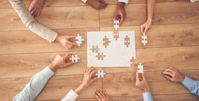 Geschäftsleute sitzen am Schreibtisch, setzen Puzzleteile zusammen, finden eine Lösung, hohe Winkelansicht.