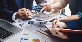 Mehrere Personen analysieren Diagramme auf Blättern und einem iPad