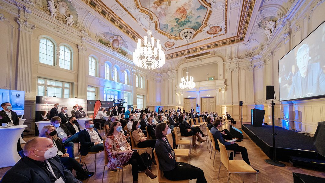 Messekongress GO.DIGITAL 2021 Keynote Ranga Yogeshwar Menschen sitzen mit Maske in einem pompösen Saal