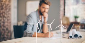 Mann blickt auf mehrere Windräder auf einem Schreibtisch 