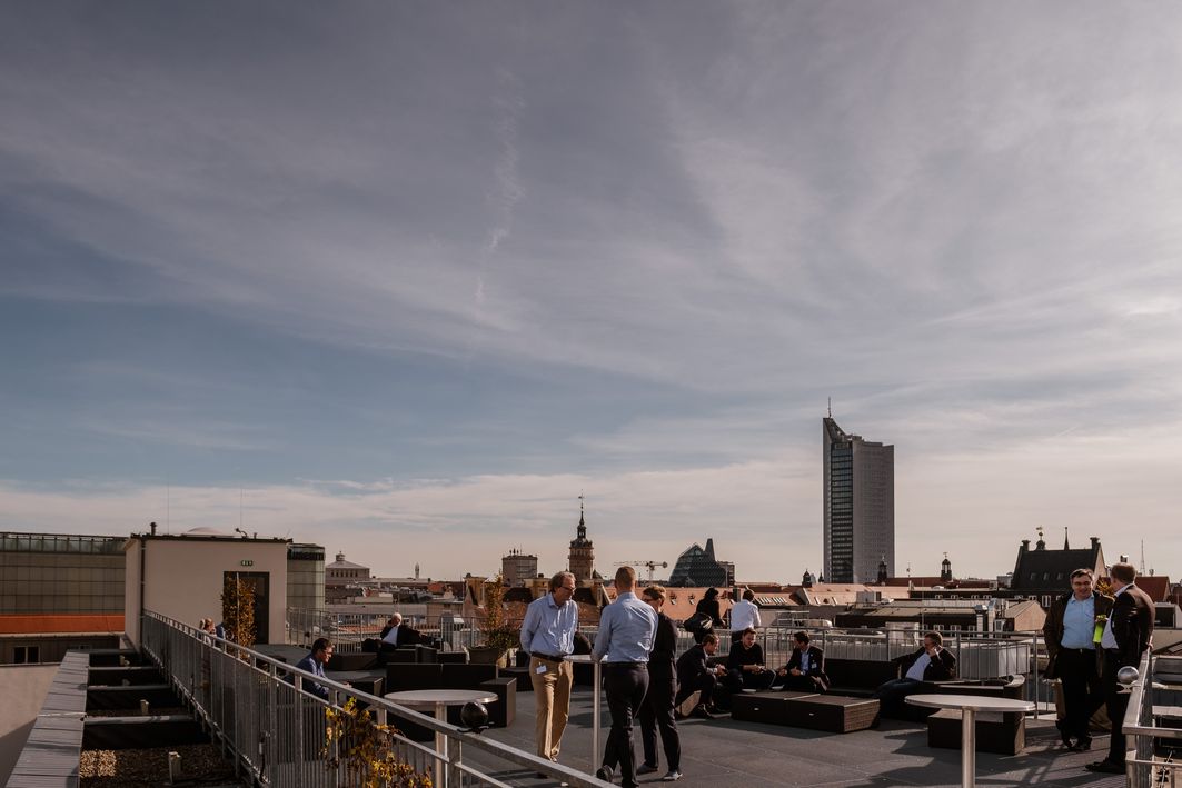 Menschen stehen auf einer Dachterrasse mit Blick über Leipzig