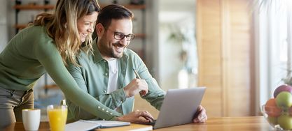 Zwei Kollegen die vor einem Laptop sitzen und gemeinsam darauf schauen