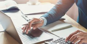 Männliche Hände arbeiten auf einem Laptop und einem Taschenrechner.