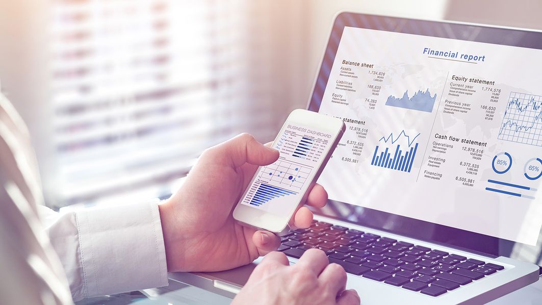 Forderungsmanagement - Finanzreporting Mann hält ein Handy in der Hand und schaut auf einen Bildschirm mit Diagrammen
