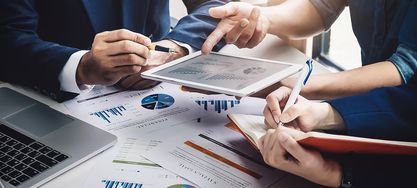 Mehrere Personen analysieren Diagramme auf Blättern und einem iPad