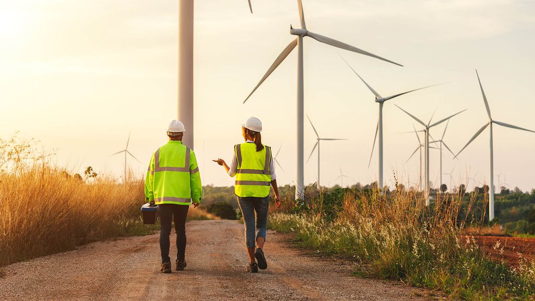 Zwei Menschen die einen Feldweg neben Windrädern entlang gehen